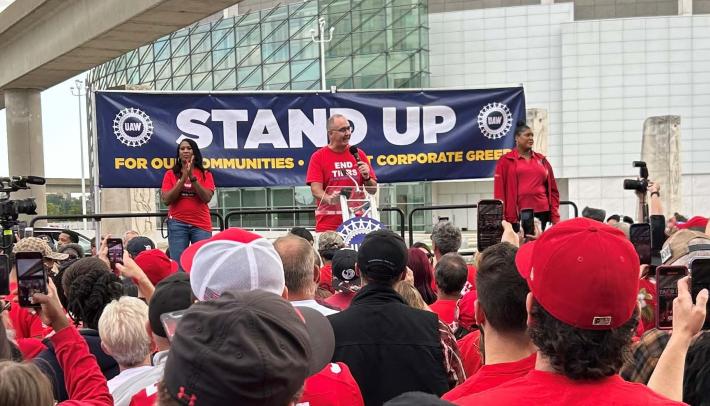 UAW members rally in front of sign that reads "stand up"