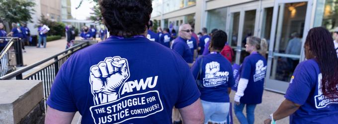 APWU members march in a rally with tshirts that say "The Struggle for Justice Continues" 