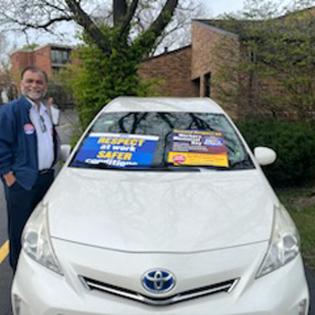 a man stands in front of his toyota car with apwu rally signs on the windshield