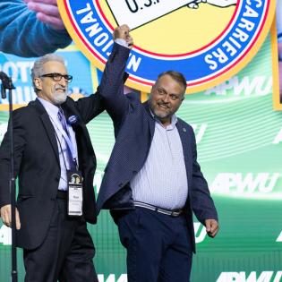 APWU President Mark Dimondstein and NALC President Brian Renfroe hold up hands together at the APWU convention