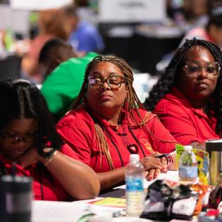 Women in red shirts watch convention proceedings. 