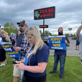 APWU members holding signs on a lawn at a rally that say "Respect at work"