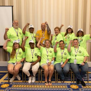 APWU members holding up fists and wearing green COPA shirts in a hotel conference center. 