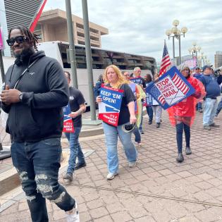 postal workers marching in a rally line holding signs that say don't delay our mail